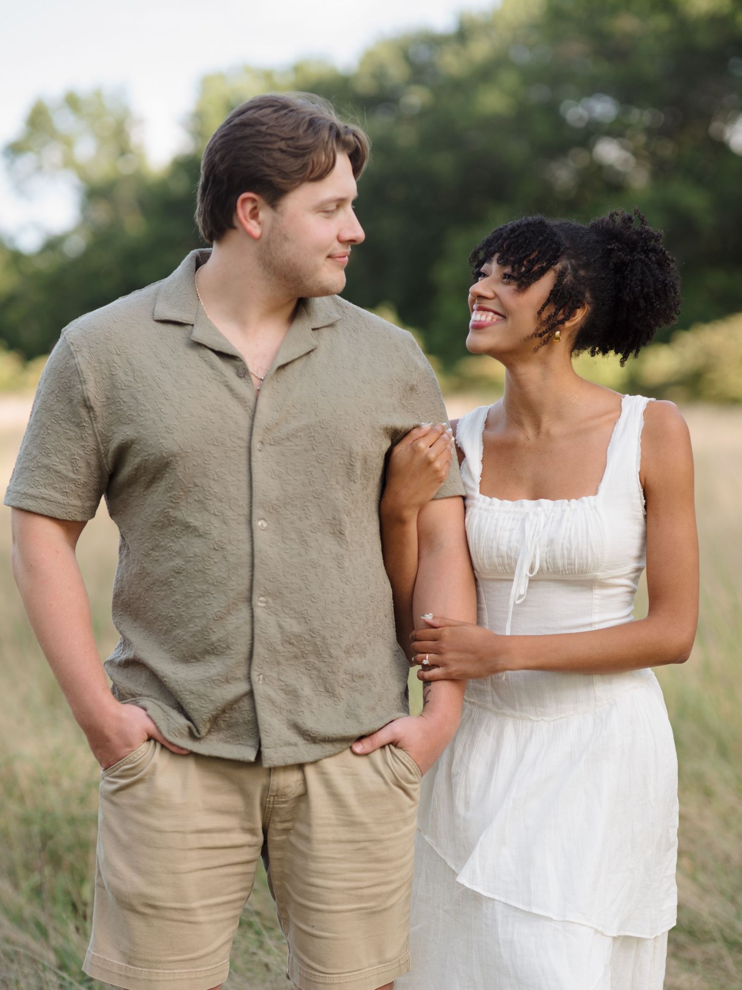 Candid couple photo shoot in a golden grassy field wearing casual summer outfits.