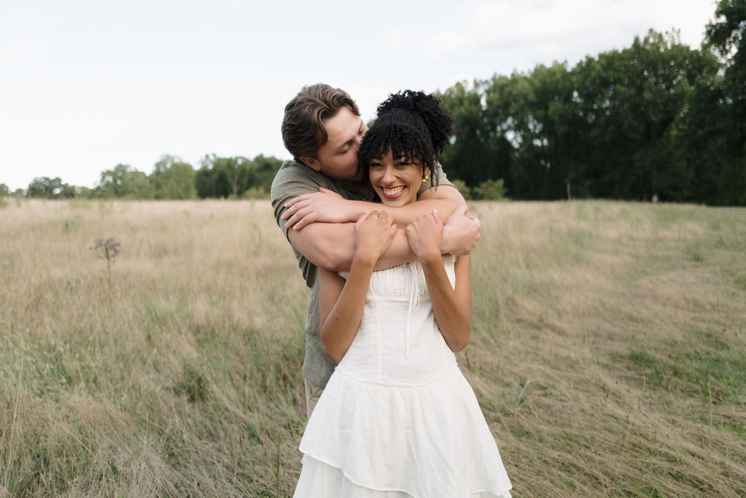 A romantic couple embraces in a field of tall grass during golden hour.