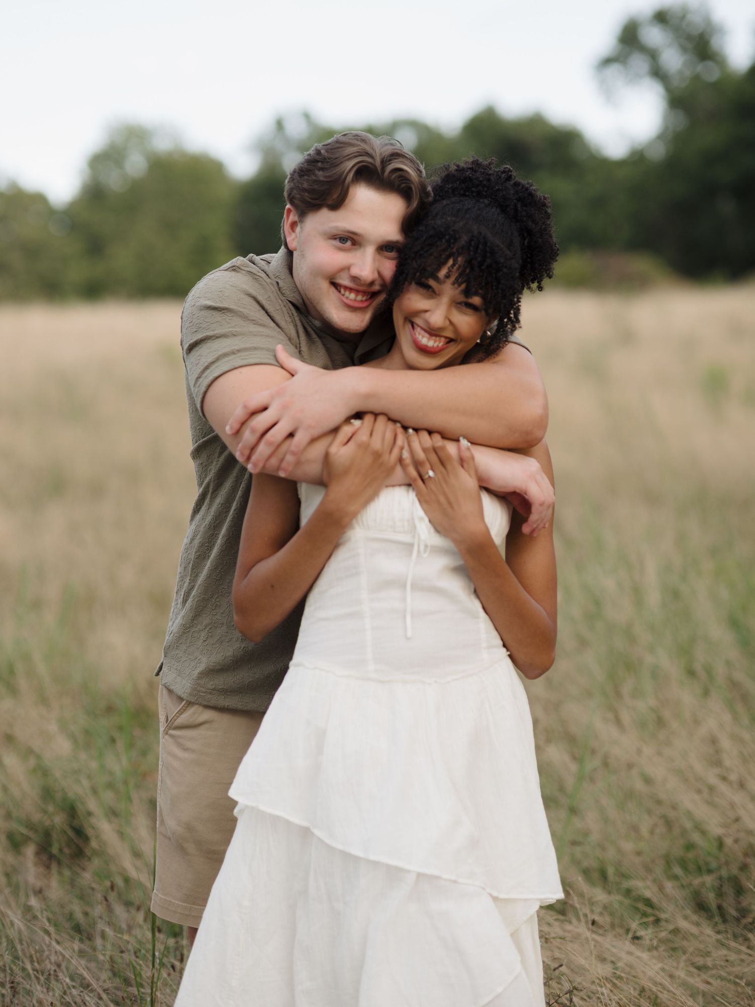 A romantic couple embraces while standing in a golden field during sunset.