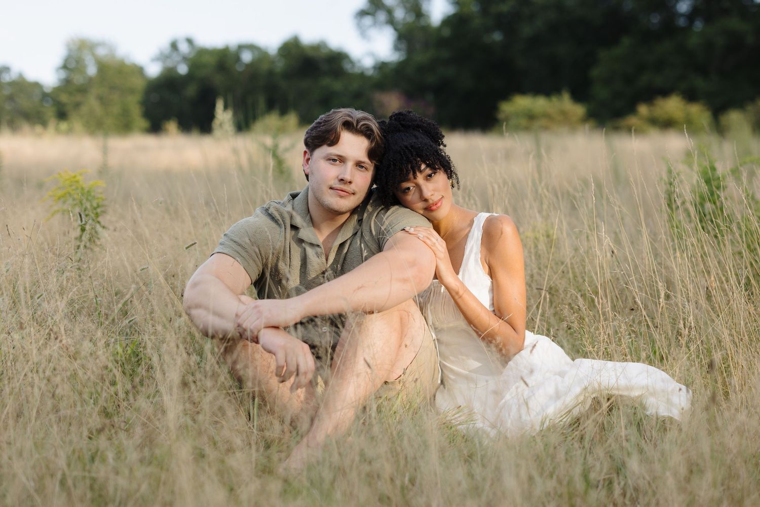 Couple photographed from a distance embracing in tall grass during golden hour.