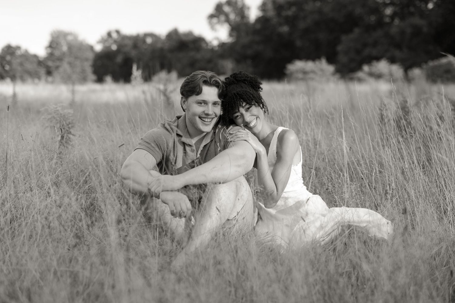 Couple relaxes in tall grass meadow together during romantic outdoor photoshoot.