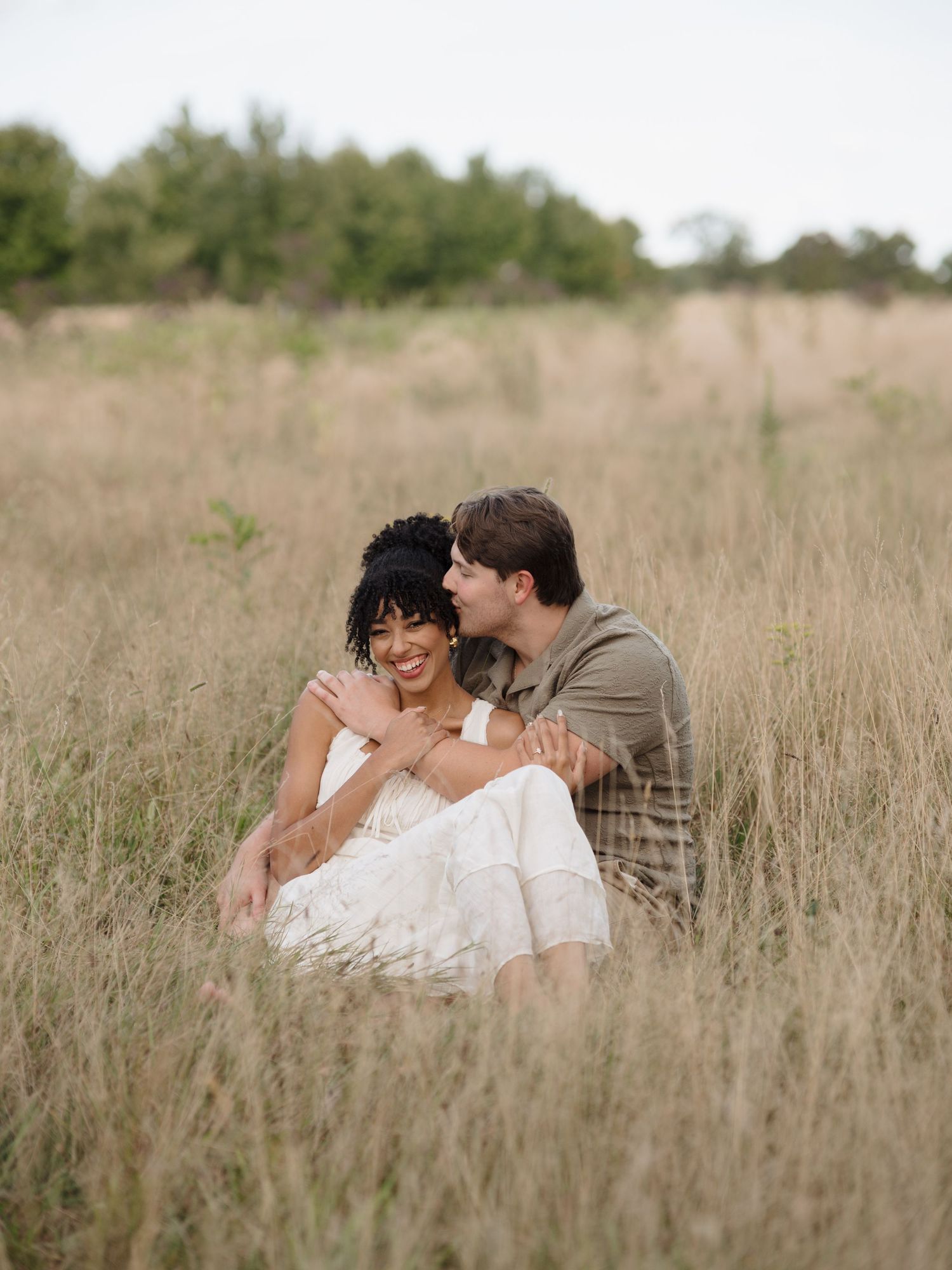 A romantic couple share intimate moments while lying together in tall golden grass during a photo session.