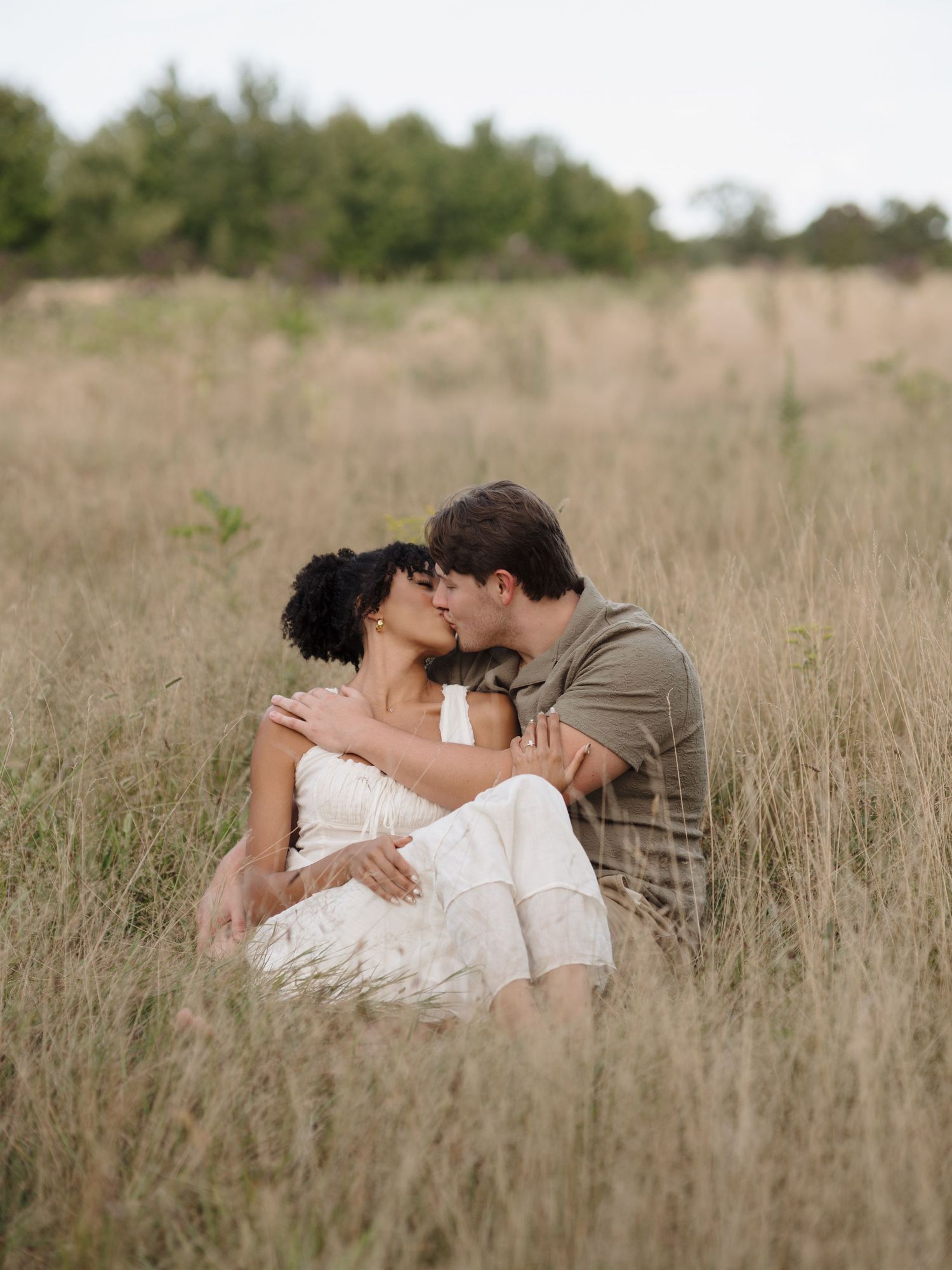 Romantic couple lying together in a tall grass field during an outdoor photo shoot.
