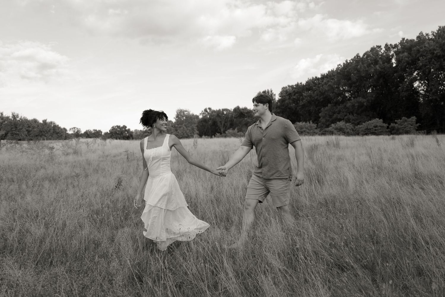 Black and white portrait of a couple walking through a serene meadow landscape.