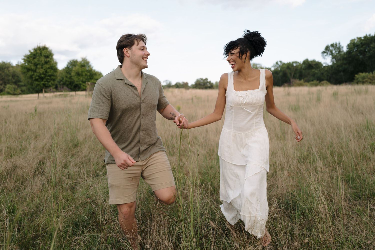 A couple in casual attire playfully interacts in a rustic field setting.
