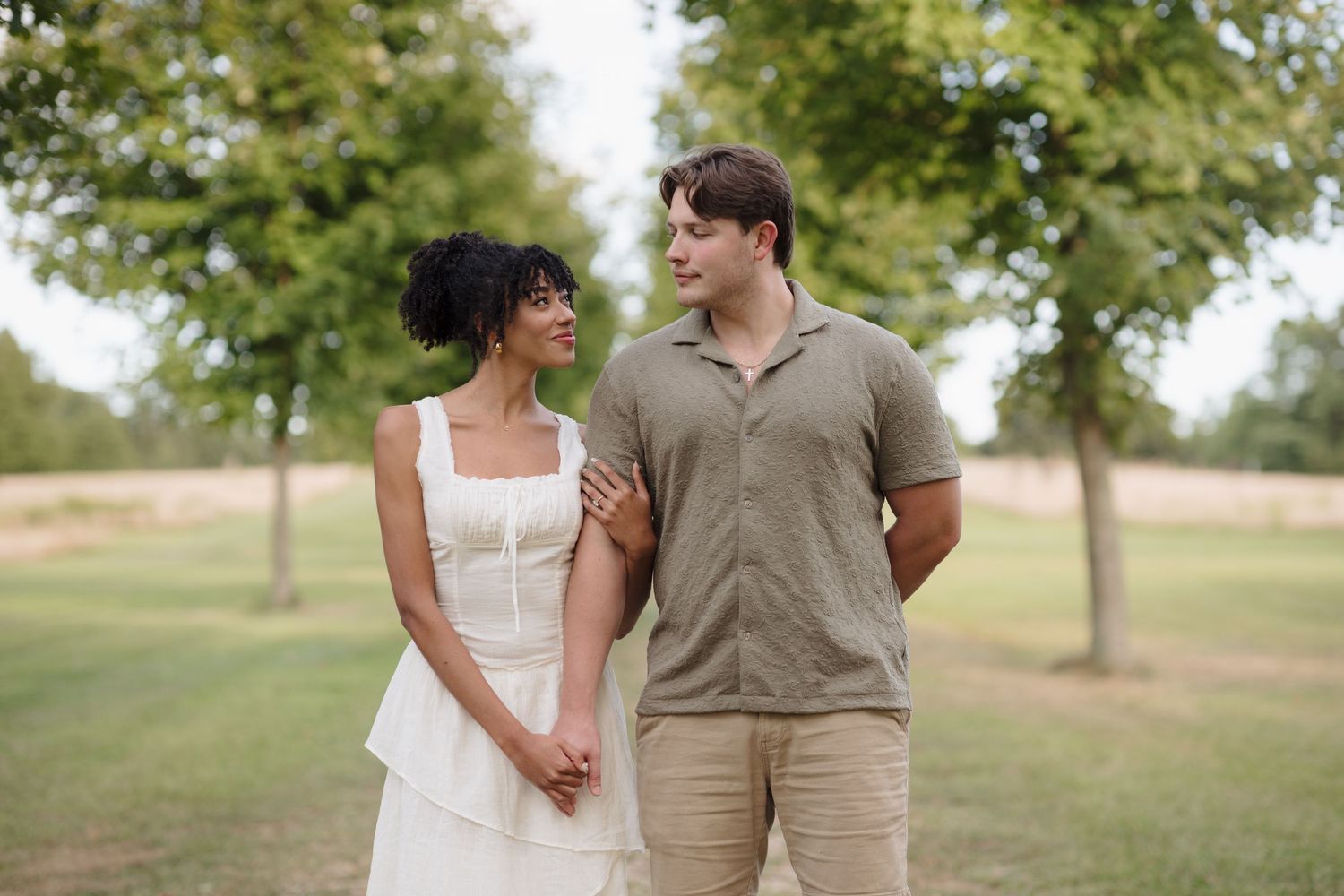 A couple shares a romantic moment in a pastoral setting with trees during a photo session at golden hour.