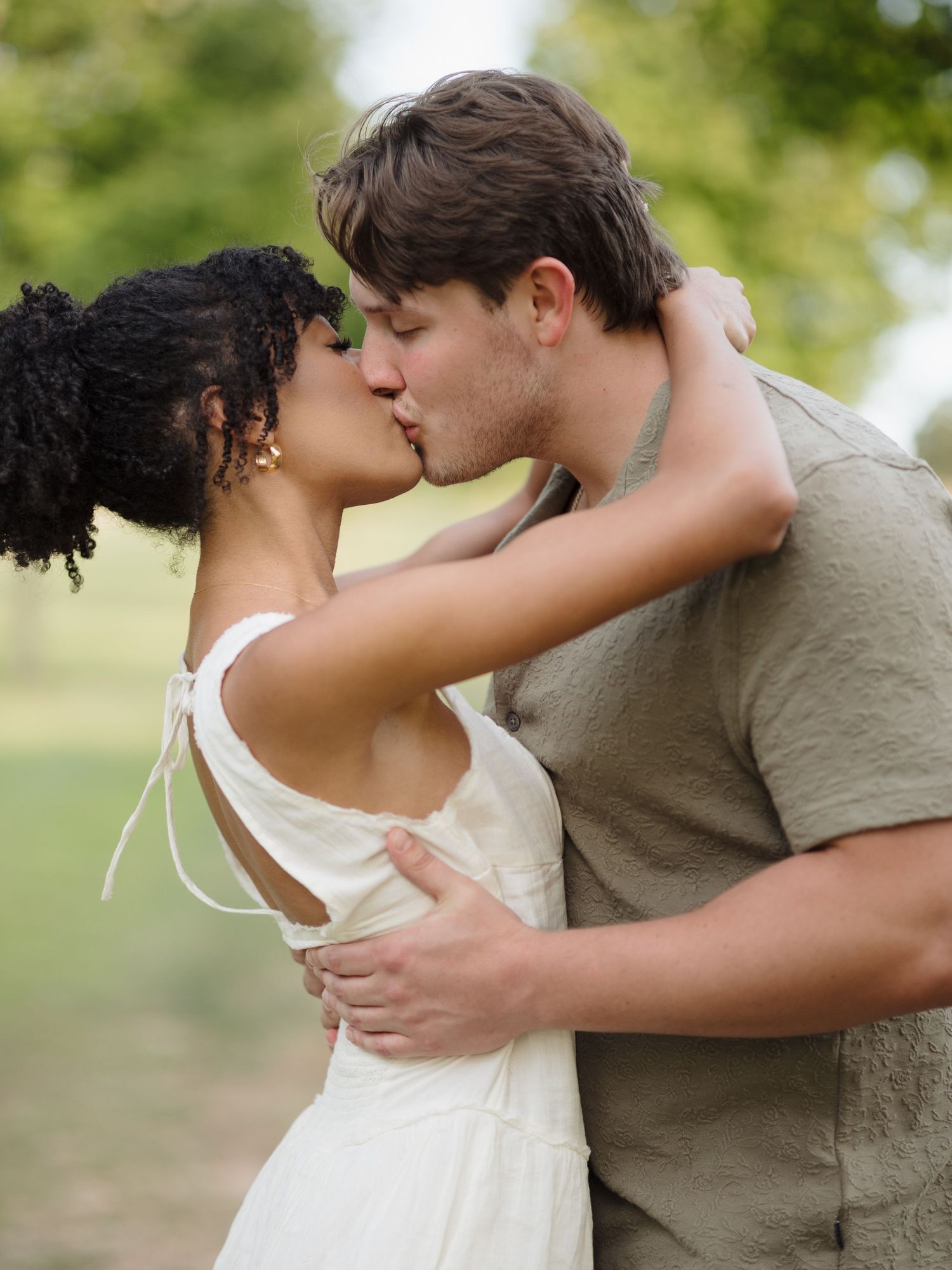 An intimate moment between a couple in white dress and casual wear outdoors.