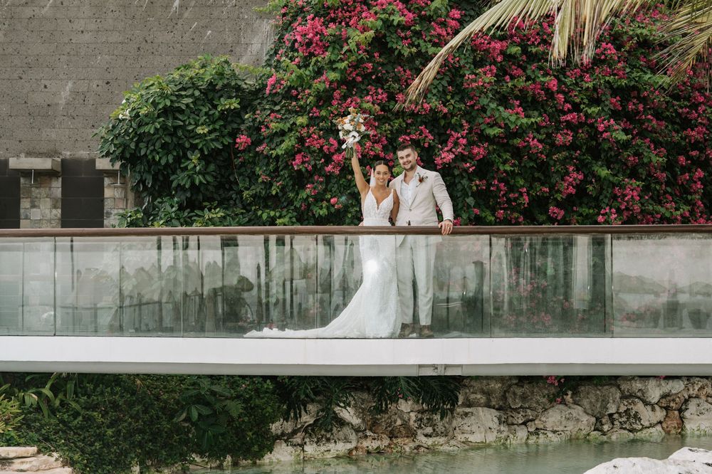 Wedding couple poses along stone wall with vibrant pink bougainvillea flowers creating a romantic garden backdrop.