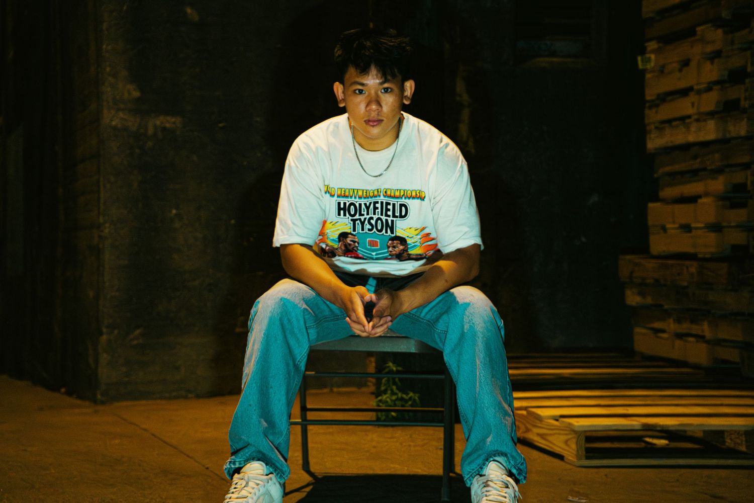 Person seated on dark chair wearing white t-shirt and blue jeans.