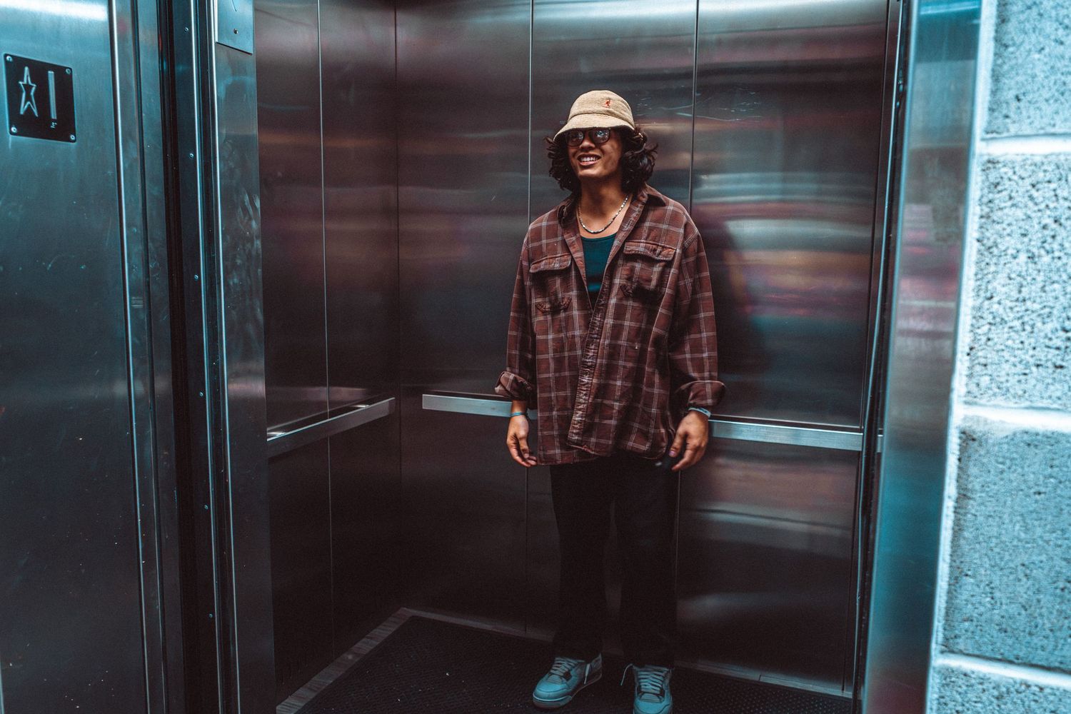 Person wearing plaid shirt and bucket hat standing in elevator.