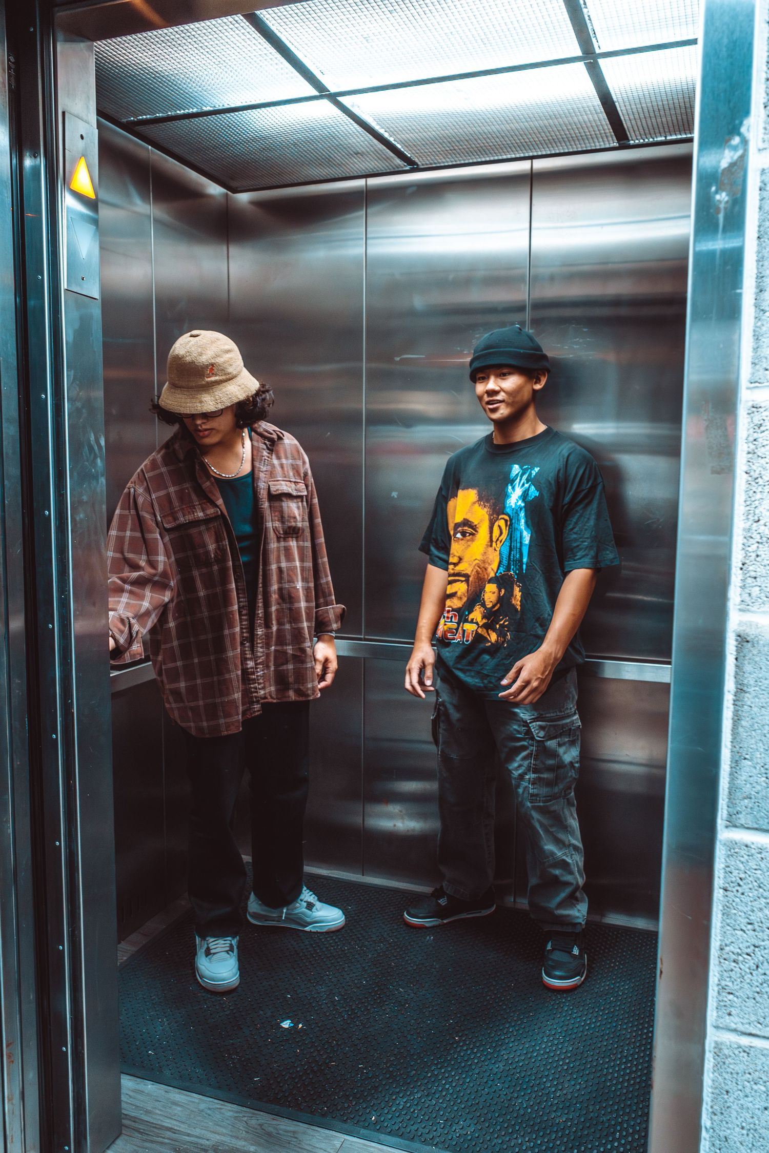 Two people standing in elevator wearing casual streetwear.