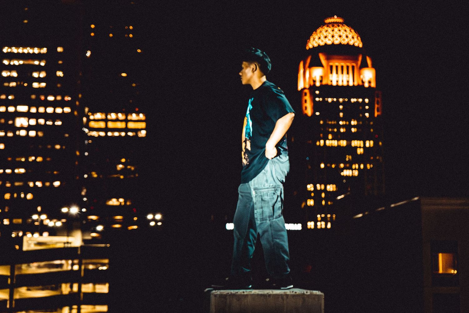 Person performing against illuminated city skyline at night with orange-lit buildings in background.