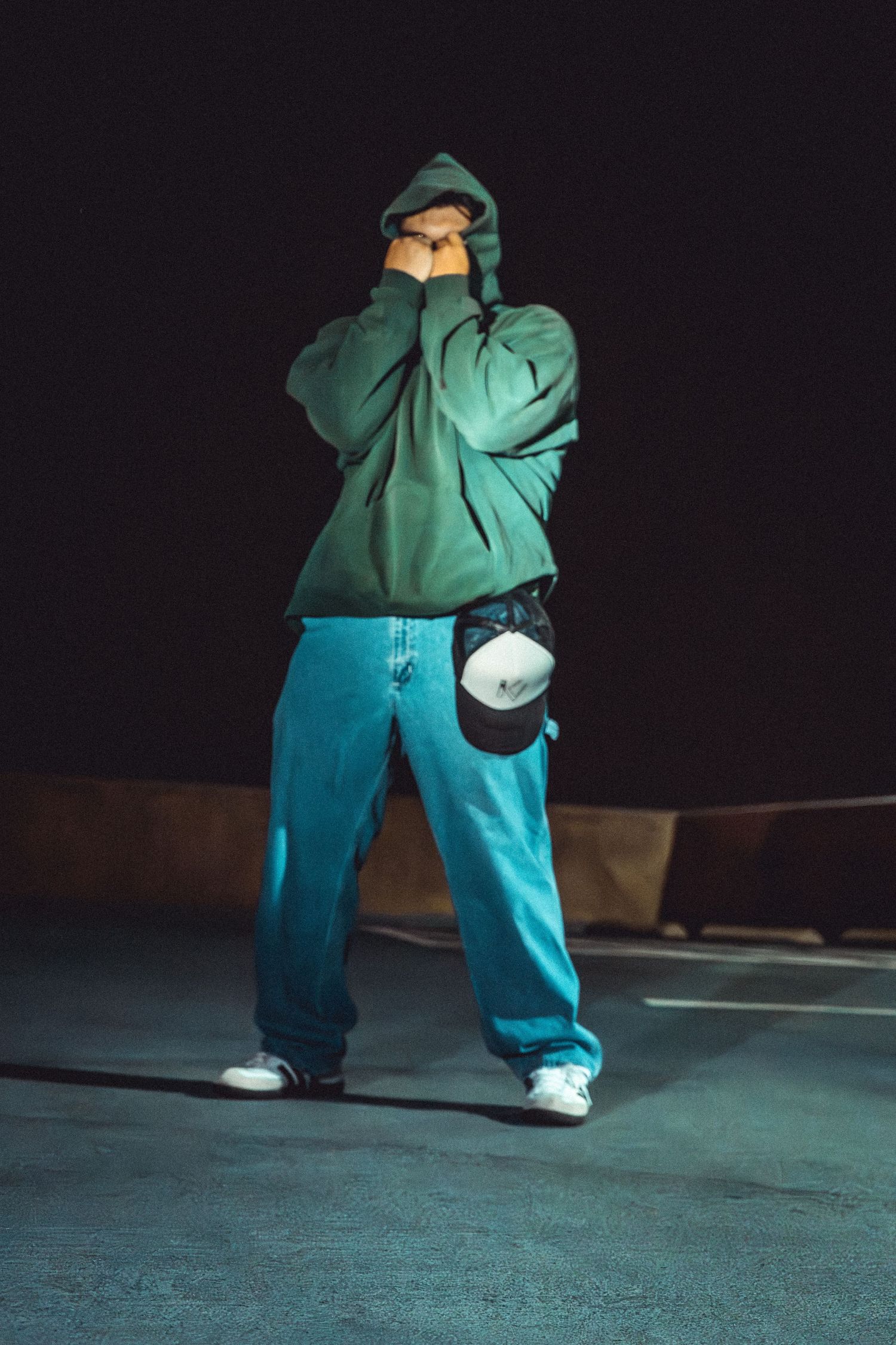 Person in turquoise clothing performing dance moves against dark background.