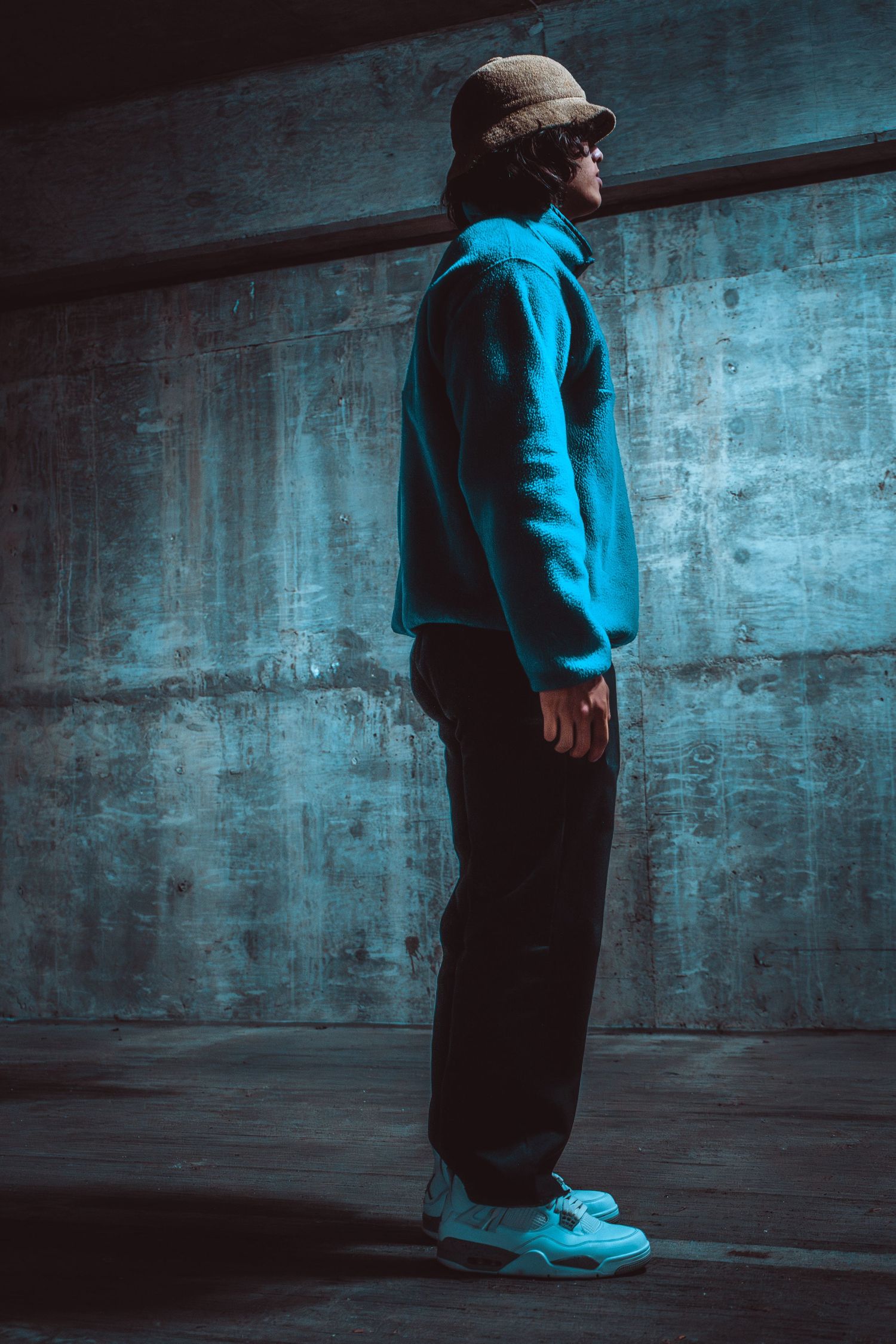 Figure standing against concrete wall in moody blue lighting.