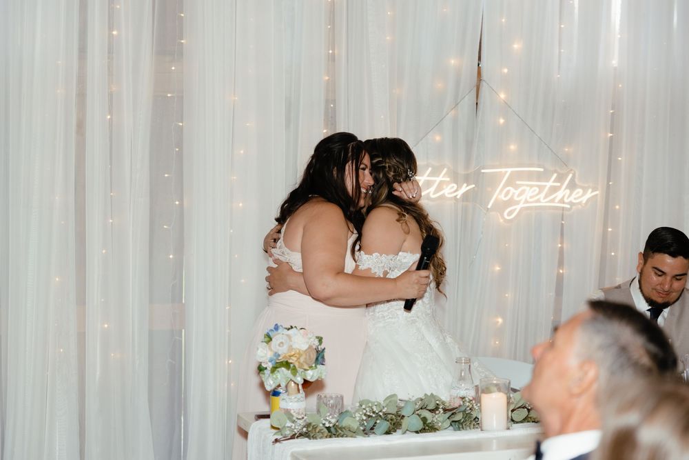 Two people share a romantic first dance at their wedding reception surrounded by white curtains and floral decorations.