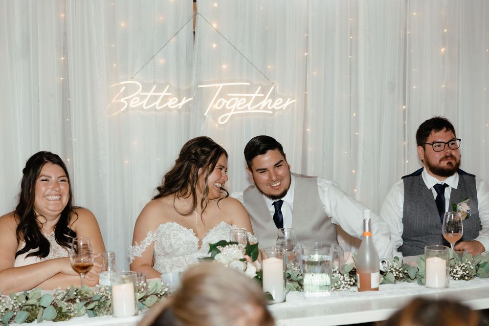 Wedding party seated at a long table during reception with white floral centerpieces and decor.