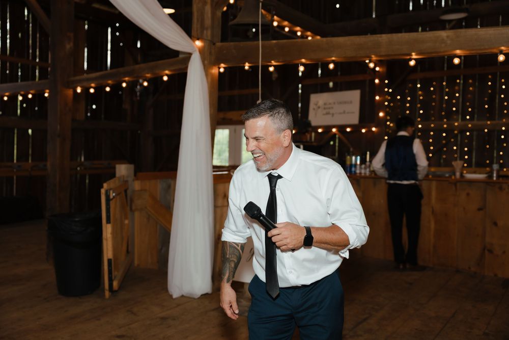 Wedding guest dancing enthusiastically in a rustic barn venue with twinkle lights.