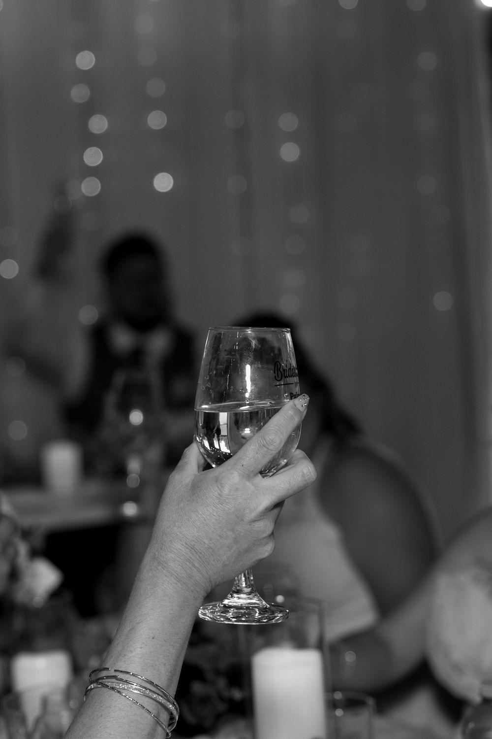 Multiple hands raise wine glasses in a toast against a dark background with bokeh lights.