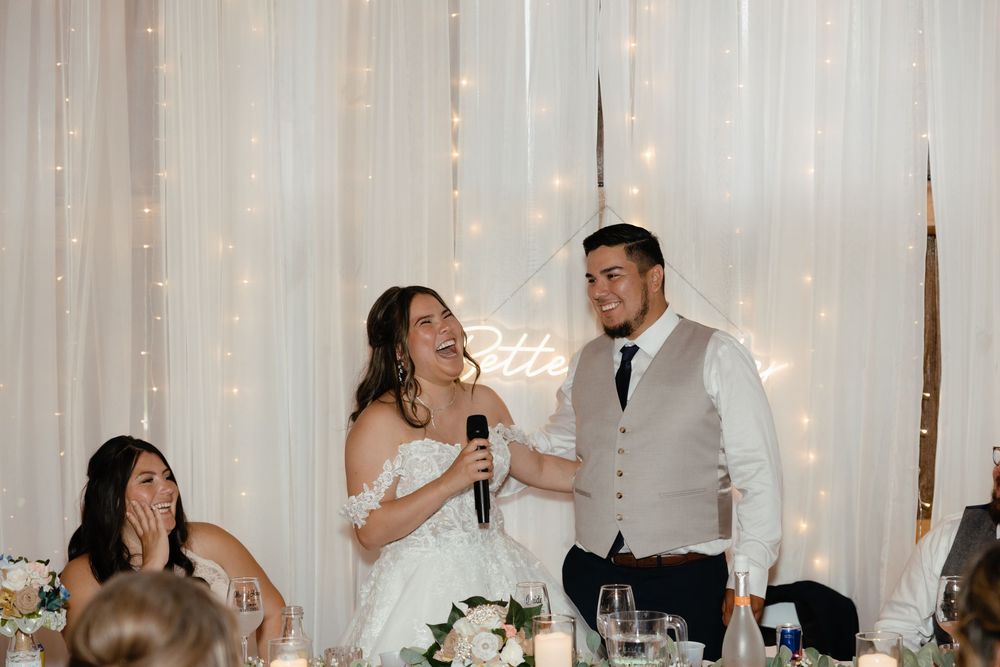 Joyful celebration during wedding reception speeches at an elegantly decorated venue with twinkle light backdrop.
