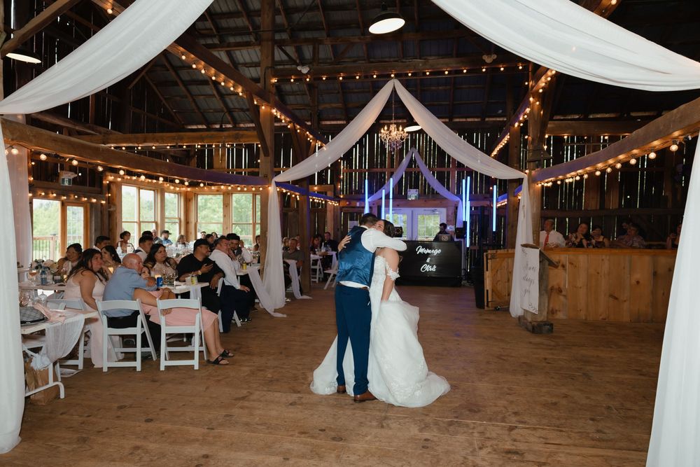 A rustic barn wedding reception space decorated with white drapes and string lights creating an elegant atmosphere.