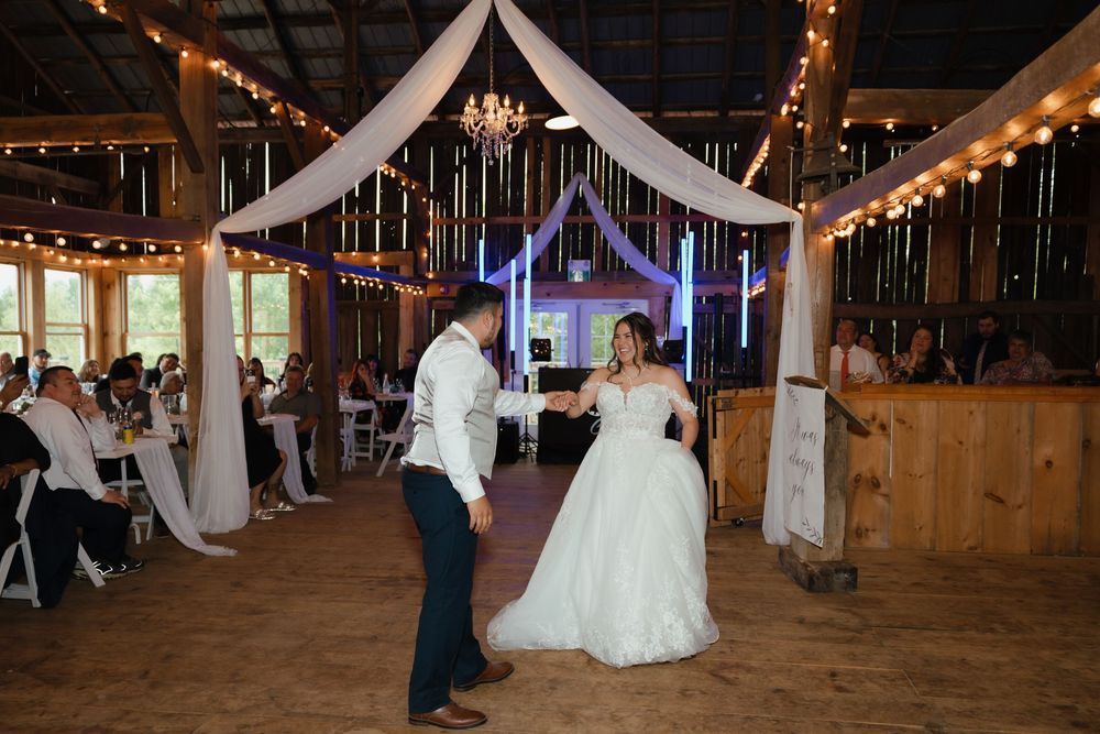 Couples dance together during reception in a barn decorated with twinkling lights and white fabric decor.