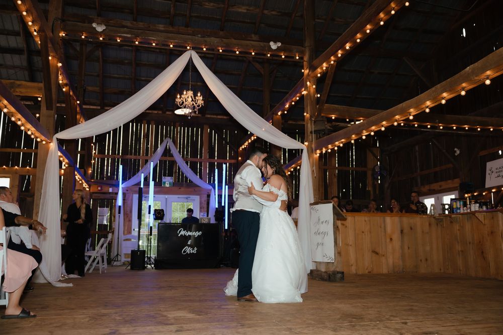 Dancing at a rustic barn wedding reception with string lights and white fabric draping overhead.