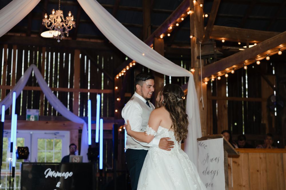 Newlyweds share a romantic dance under warm string lights and flowing white fabric draped from the ceiling.