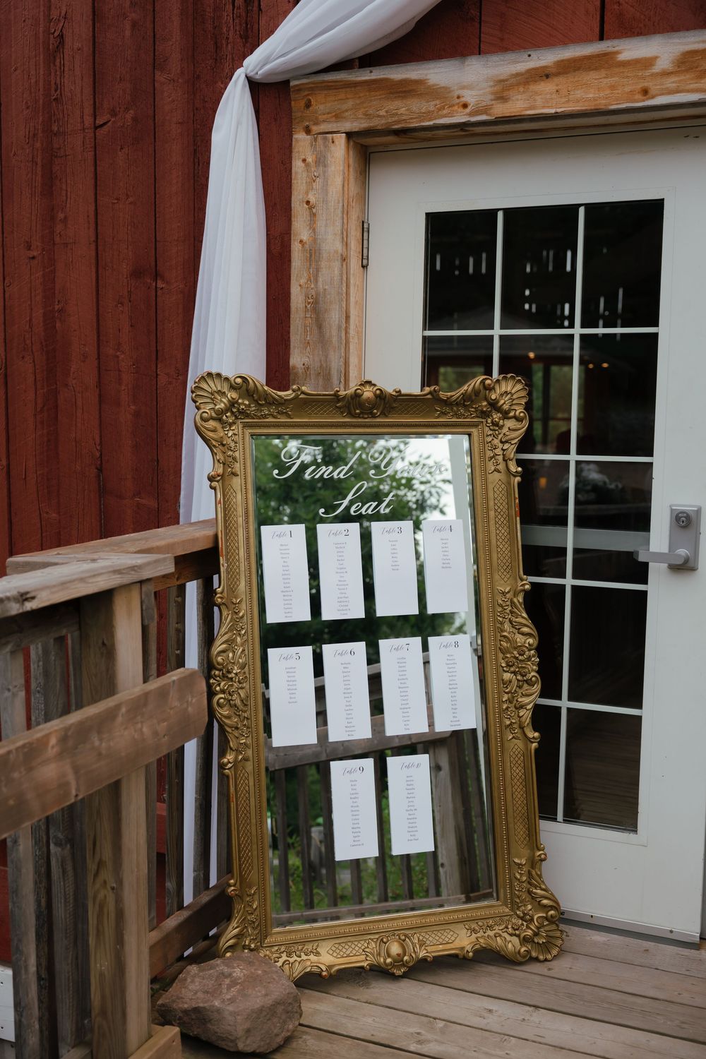 A rustic wooden porch decorated with an ornate gold picture frame and window with a seating list posted on the wall.