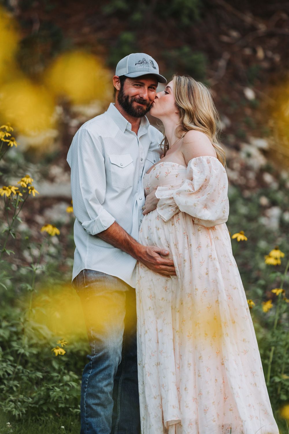 A couple embraces outdoors surrounded by yellow wildflowers as they share a tender romantic moment.