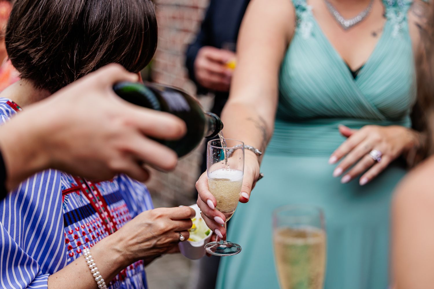 Wedding guests hold glasses of champagne in a toast line wearing turquoise and blue striped dresses at outdoor celebration.