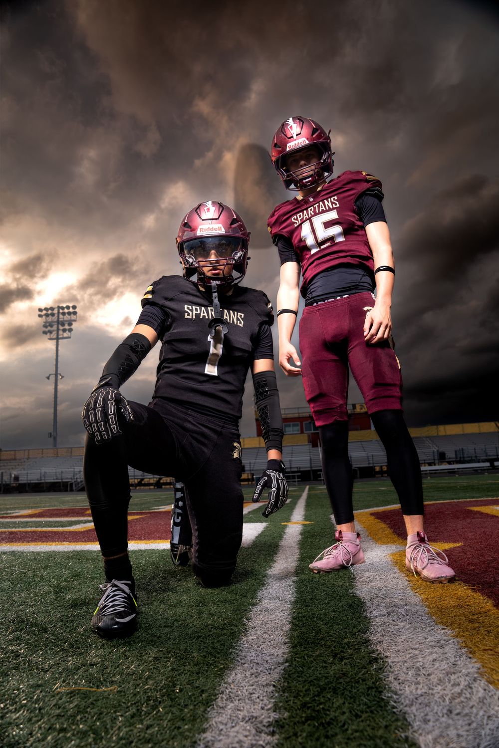 Two Spartans football players pose dramatically on field under stormy sky at night.