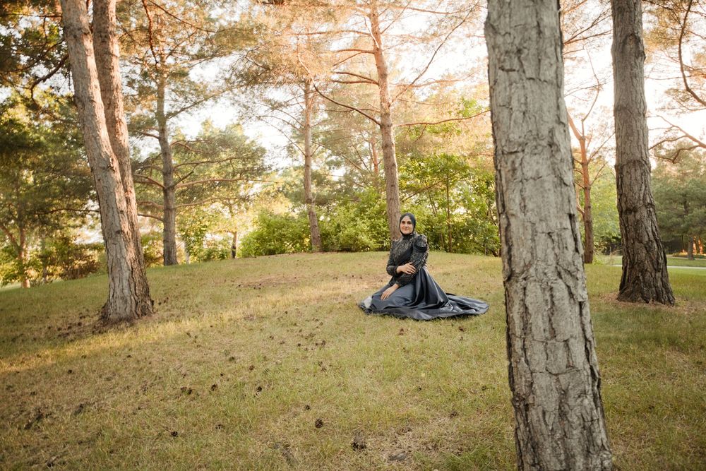 Woman in dark dress sitting on grass among tall trees in a serene autumn forest park setting.