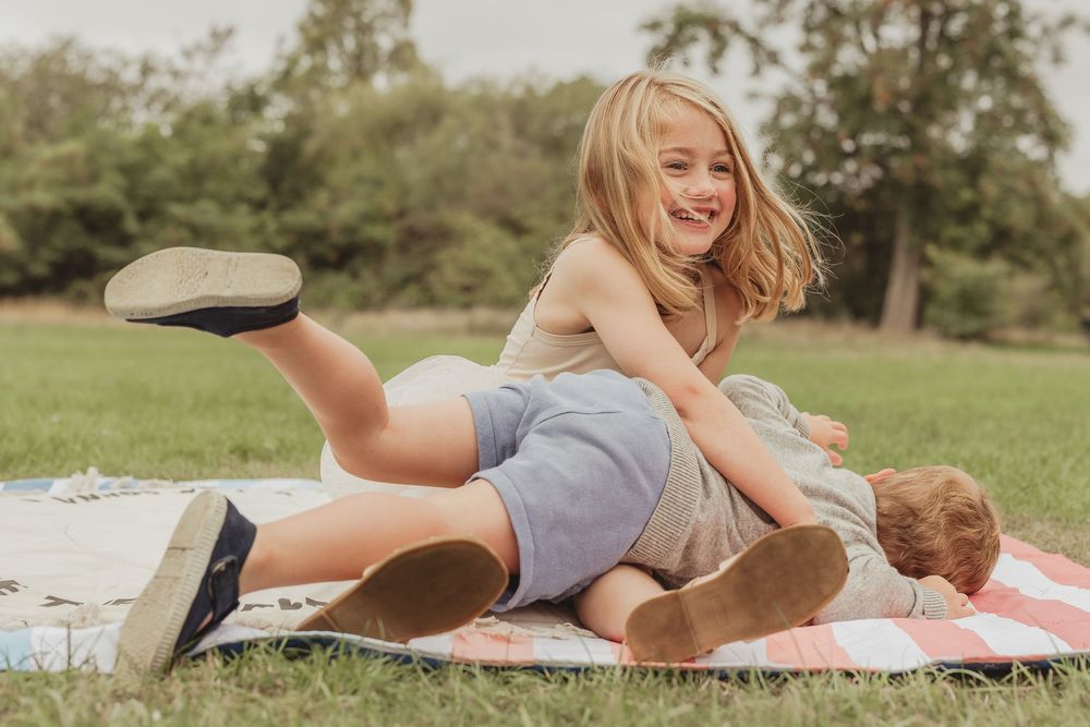 Two children lying on a picnic blanket in a grassy field on a sunny day.