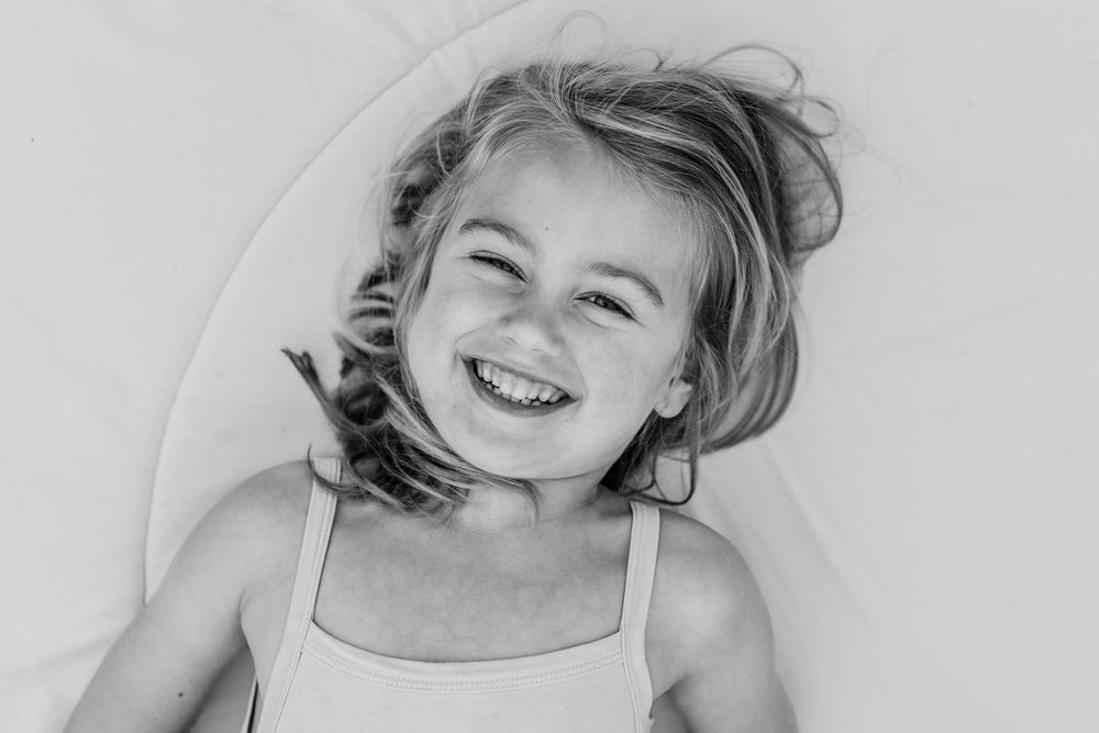 Person lying on white bedding while laughing joyfully.