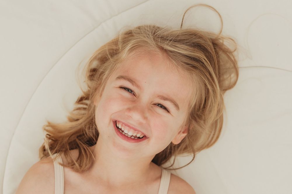 Person with blonde hair lying down and smiling against white background.