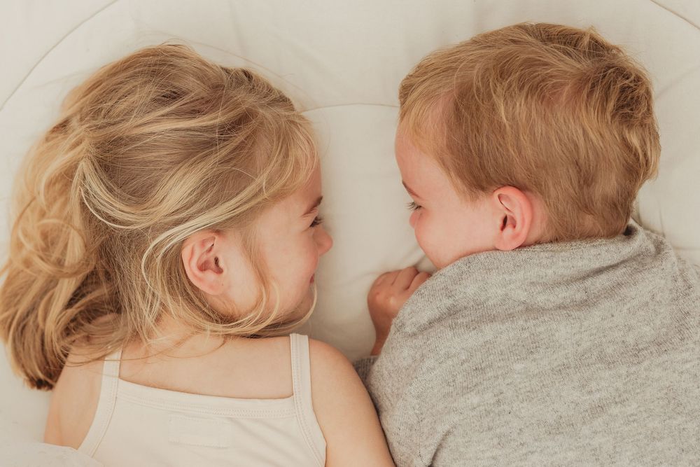 Two siblings lying close together on light colored bedding.