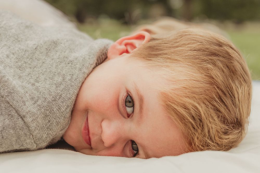 Toddler wearing grey sweater lying down and looking at camera.