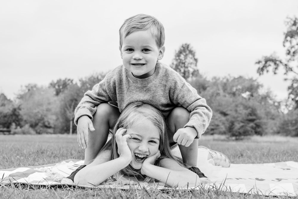 Two people playing and laughing together on a blanket outdoors.