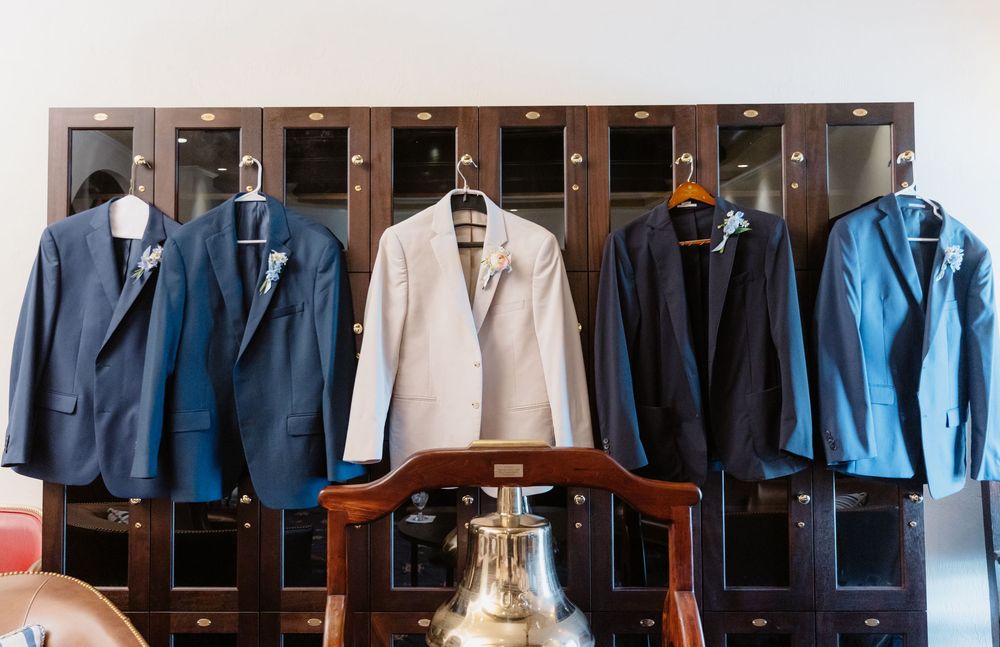 Row of navy blue and light colored formal suits hanging on display in a closet.