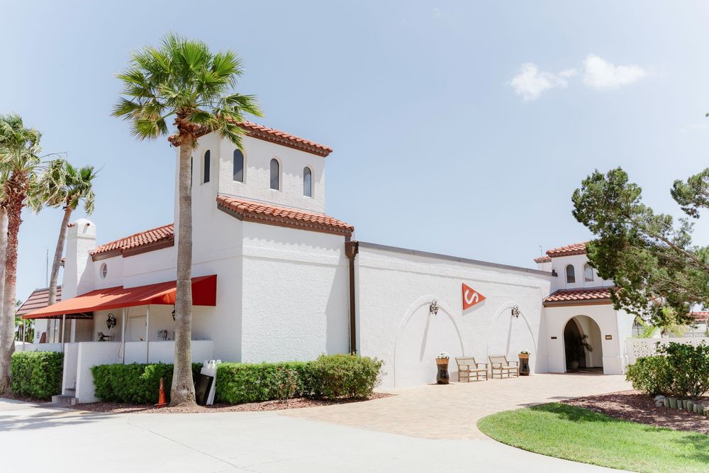 Spanish-style white stucco buildings with red tile roofs and palm trees under blue sky.