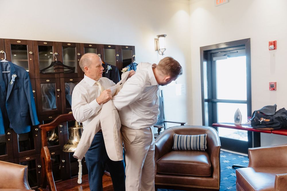 Men in formal attire getting dressed in a wood-paneled dressing room with leather seating.