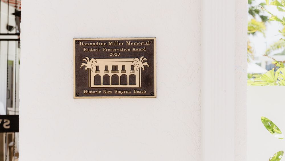 A vintage plaque mounted on a white wall displays text and decorative design elements.