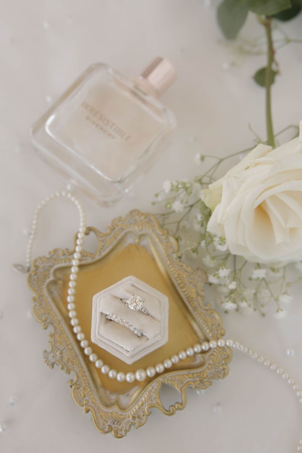 Wedding details featuring pearl necklaces and perfume bottles arranged with delicate white flowers on a light surface.
