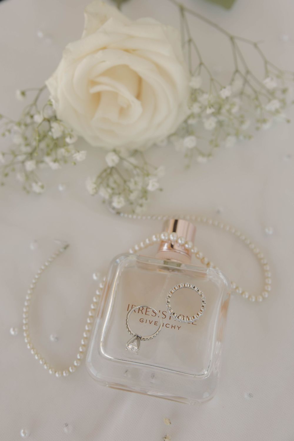 White roses and pearl necklaces elegantly arranged with perfume bottles on a light surface.