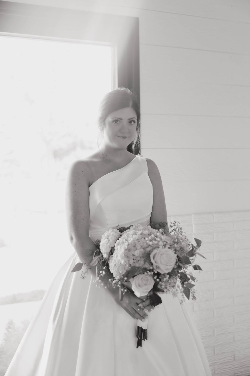 Elegant bride in white ballgown holding delicate bouquet of roses and baby's breath flowers.