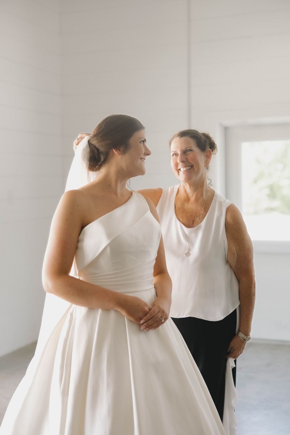 Elegant candid moments between two women in white dresses sharing laughter in a bright indoor space.