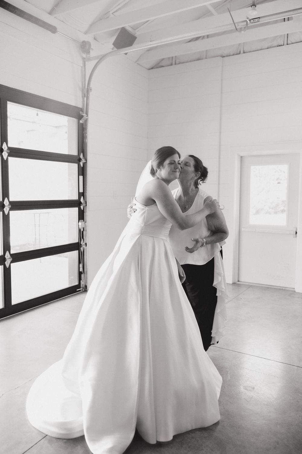 Couple in elegant white wedding attire share an intimate moment in a bright studio space.