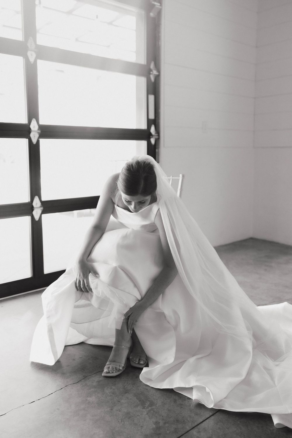 Black and white image of flowing white wedding dress fabric and heels against minimalist background.