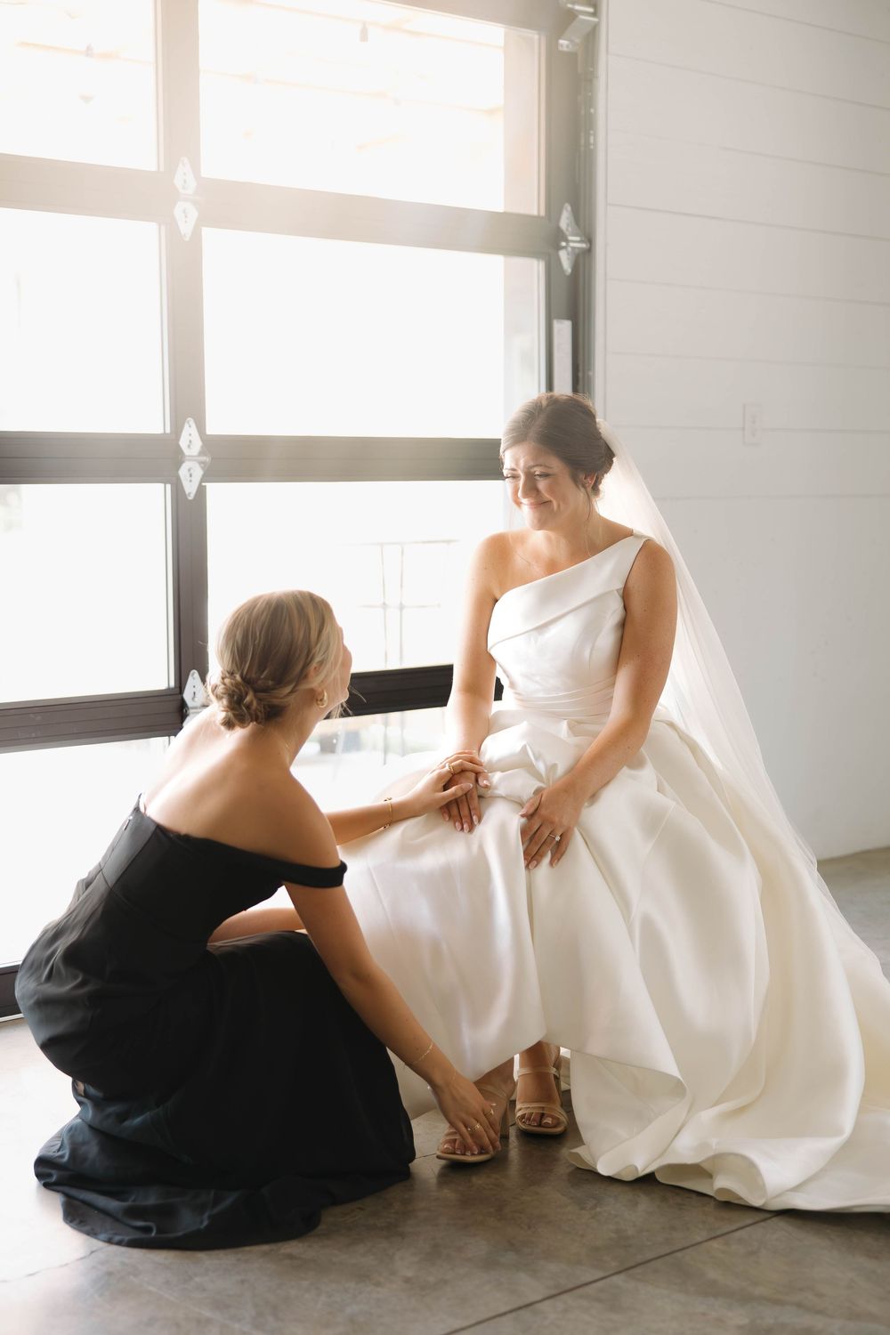 Wedding preparation scene with two people in contrasting black and white dresses sitting on a bright floor.