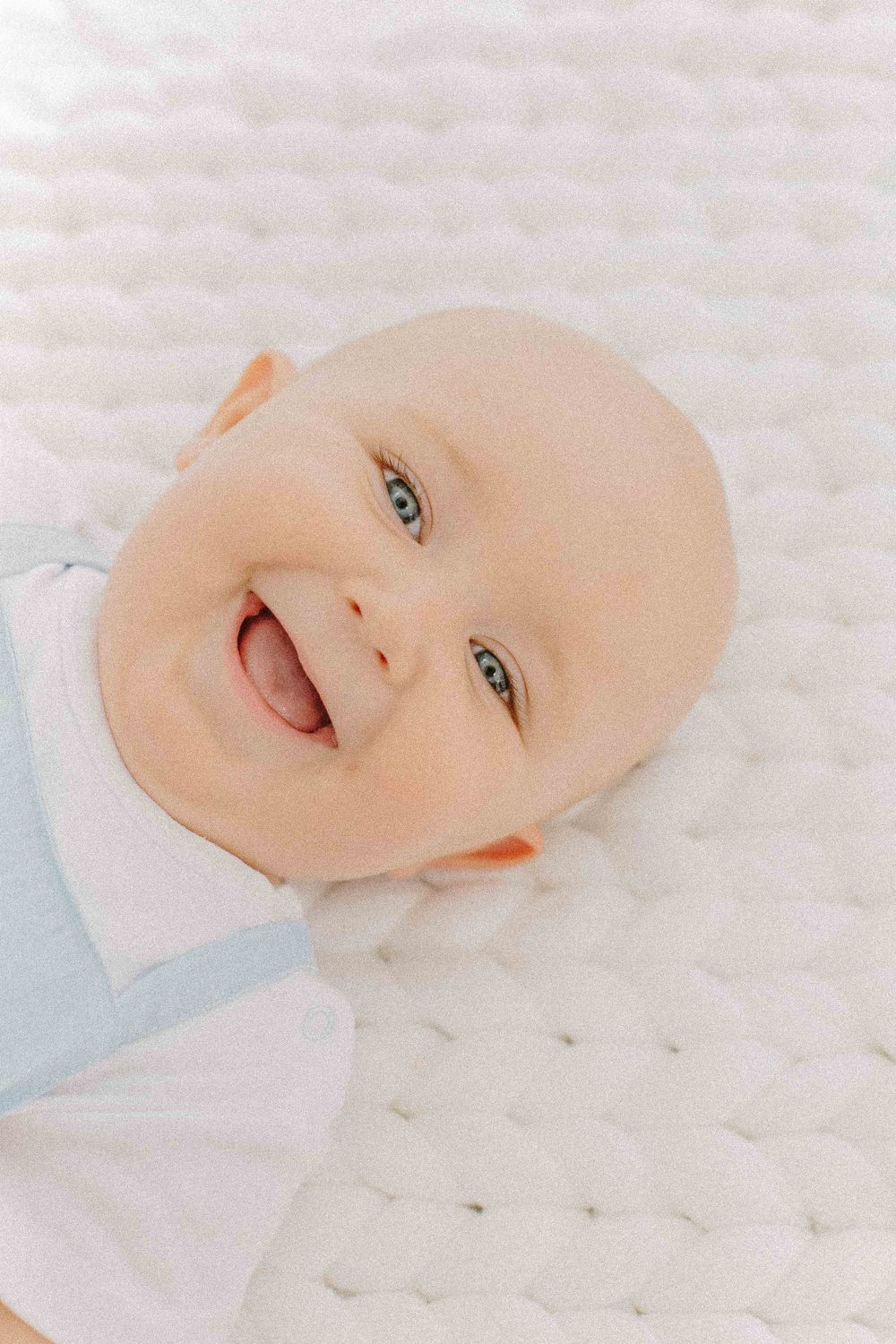 Close-up of smiling baby in light blue outfit on white textured background. Estúdio de fotografia em Alenquer